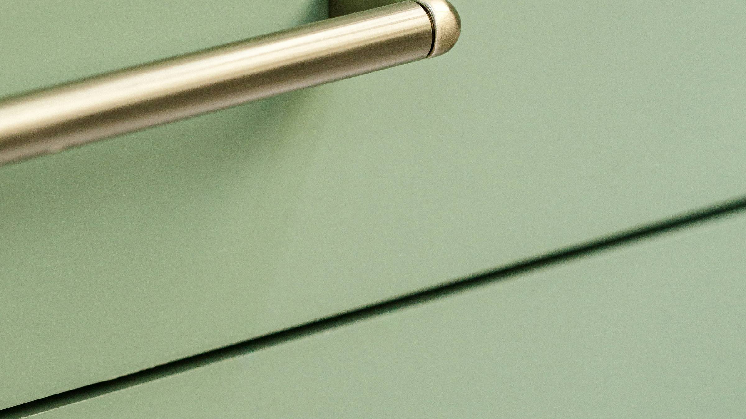 Close view of flat-panel cabinet drawer fronts in a soft green, with slim brushed metal bar pulls